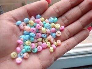 Miçanga redonda tons pasteis com letra dourada (pct c/10g)