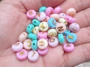 Miçanga redonda alfabeto fundo colorido tons pasteis com letra dourada(pct c 10 g)